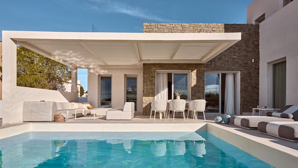 Un espace piscine extérieur moderne, agrémenté d’un mur en pierre, de mobilier blanc et d’un coin salon abrité.