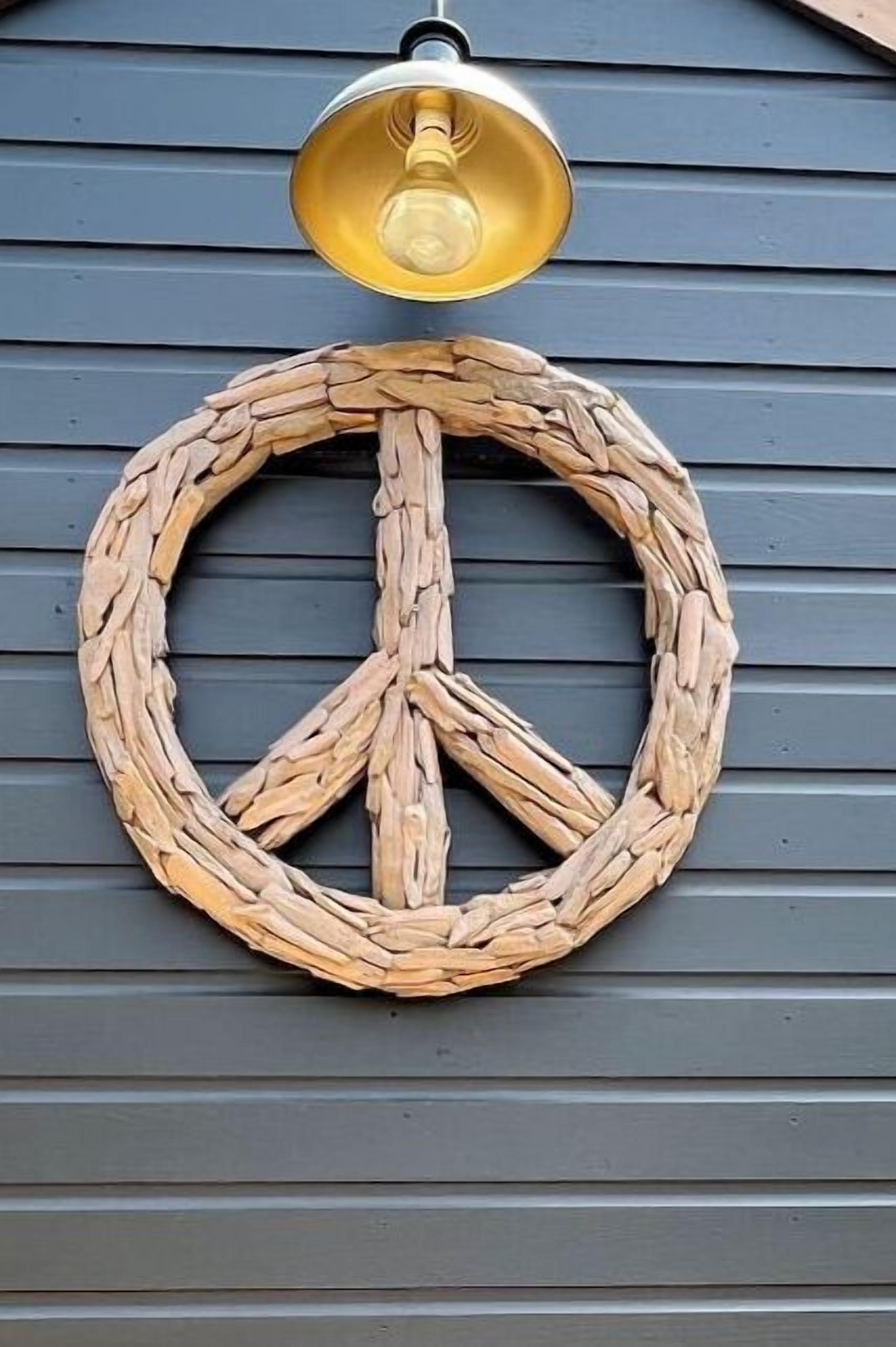 Une couronne en forme de symbole de la paix, faite de bois, est accrochée à un mur bleu foncé, et une lampe suspendue se trouve au-dessus.