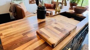 A kitchen with a wooden countertop, a sink, and cabinets. There are windows and a plant in the background. - 🌾Welcoming Tiny Home! Downtown & Beachy☀️ (Guilford)