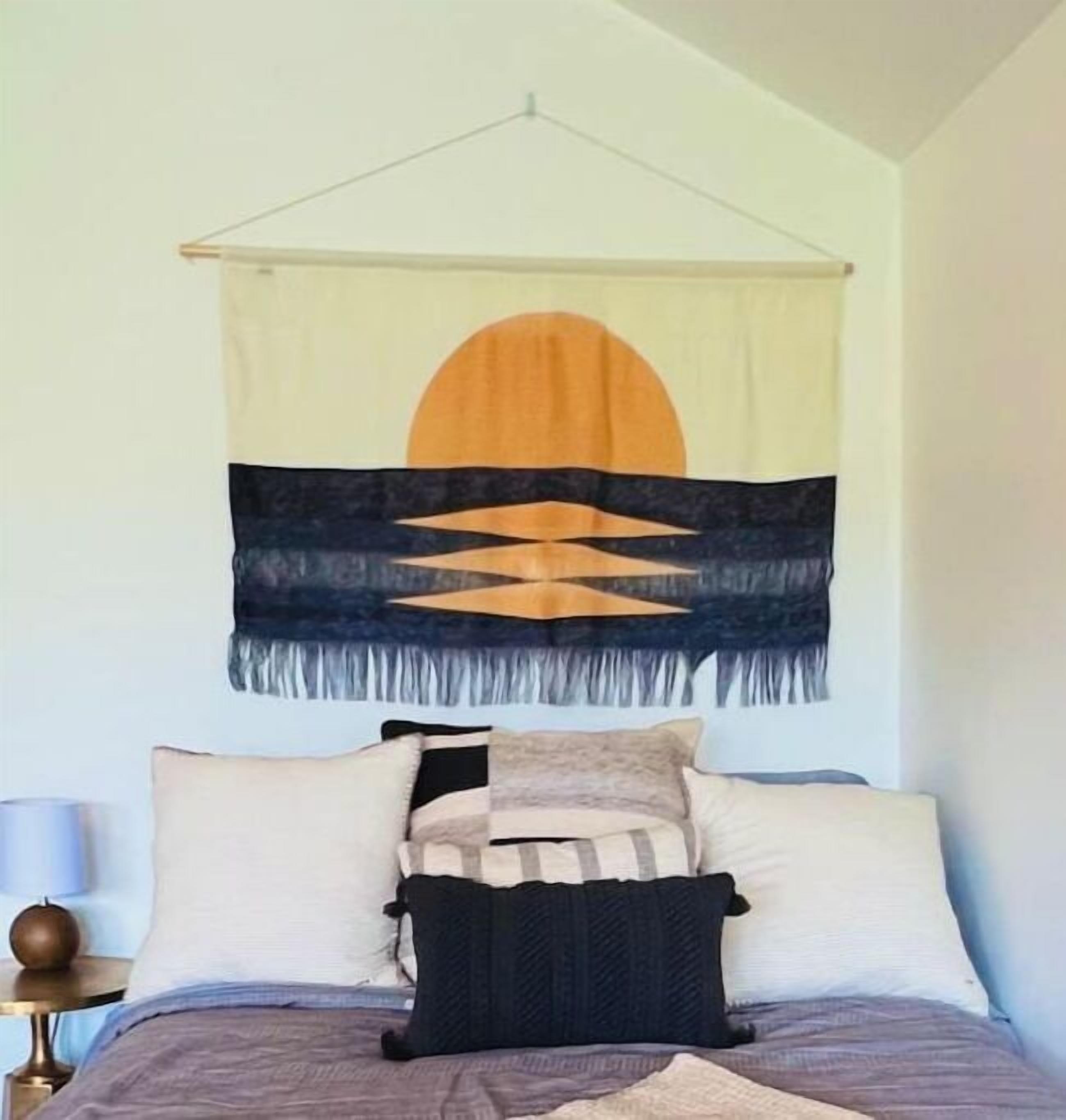 Un lit avec une tête de lit, une tapisserie murale et une table de chevet avec une lampe.