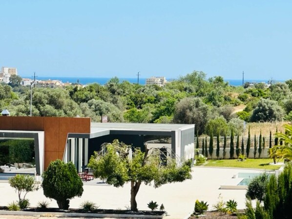 A modern building with a flat roof, surrounded by lush greenery and a clear view of the sea.