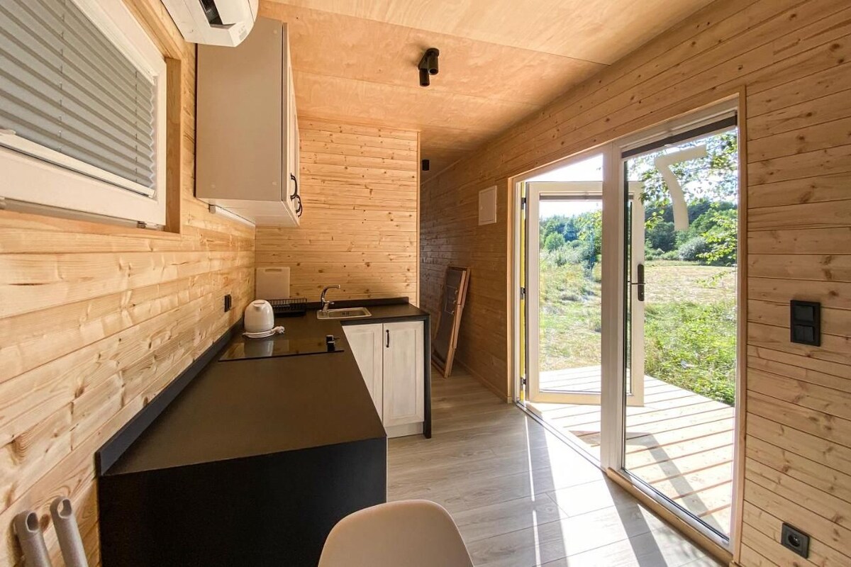 Une cuisine moderne avec des murs en bois, un plan de travail noir et une porte-fenêtre coulissante donnant sur un espace extérieur.