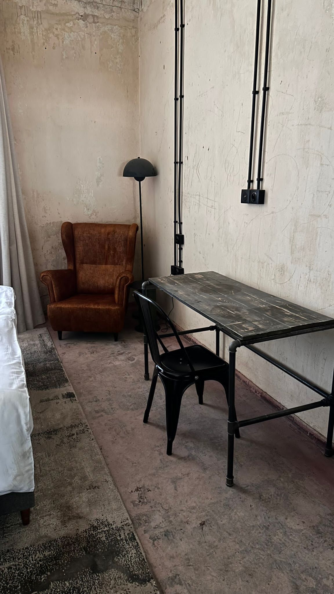 Una habitación con una larga mesa de madera, dos sillas negras, un sillón marrón y una lámpara de pie.