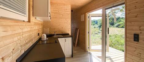 A modern kitchen with wooden walls, a black countertop, and a sliding glass door leading to an outdoor area.