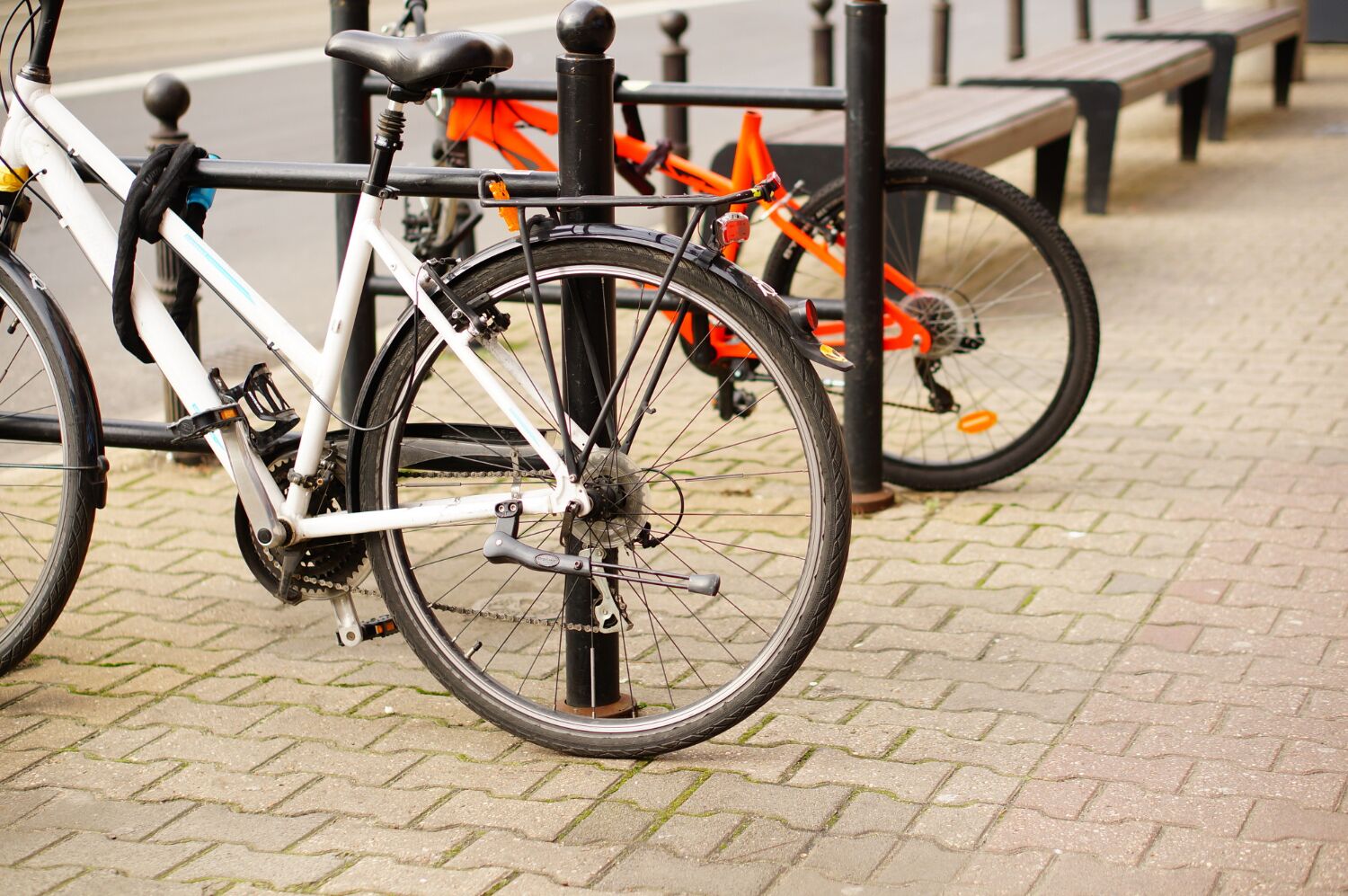 Ein Fahrrad steht neben einem Metallgestell, im Hintergrund eine Bank und ein weiteres Fahrrad.