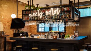 Un espace bar avec un néon, des étagères remplies de bouteilles et de verres, ainsi qu’une machine à café.