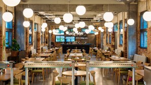 Un restaurant spacieux avec de hauts plafonds, des murs en briques apparentes et des luminaires suspendus de forme arrondie. Les tables sont disposées en forme de U autour d’un bar central.