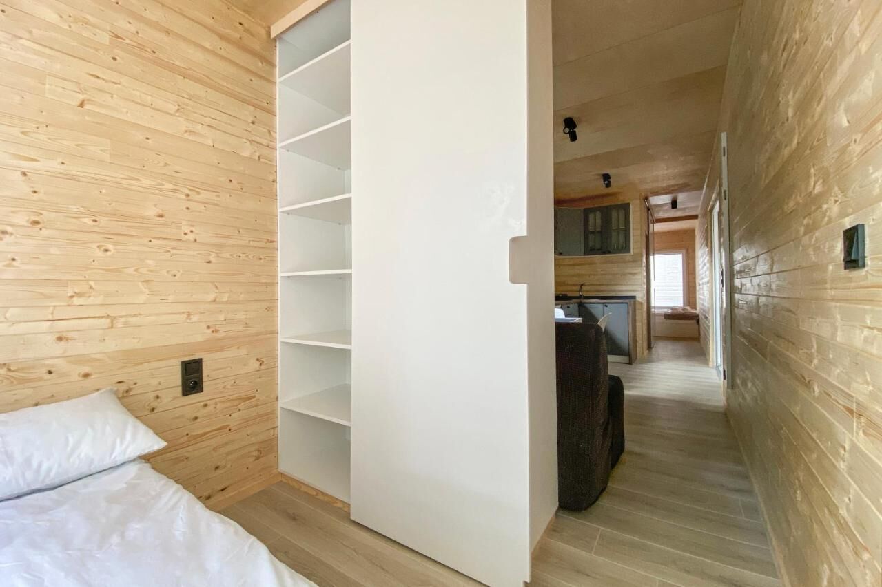 Un interior de madera con una cama, un armario blanco y una zona de cocina.