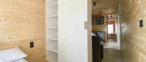 A wooden interior with a bed, a white wardrobe, and a kitchen area.