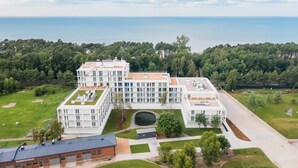 Un bâtiment moderne à plusieurs étages, doté d’un toit plat, entouré d’une pelouse bien entretenue et avec une étendue d’eau en arrière-plan.