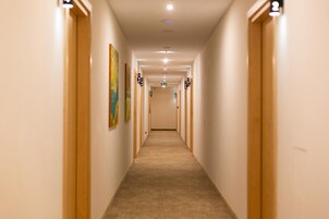Un largo y estrecho pasillo con puertas a ambos lados, placas con números sobre cada puerta, y suelo cubierto de alfombra.