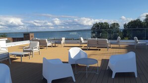 Une terrasse sur le toit, dotée de mobilier d’extérieur blanc, d’une balustrade en verre et offrant une vue sur la mer.