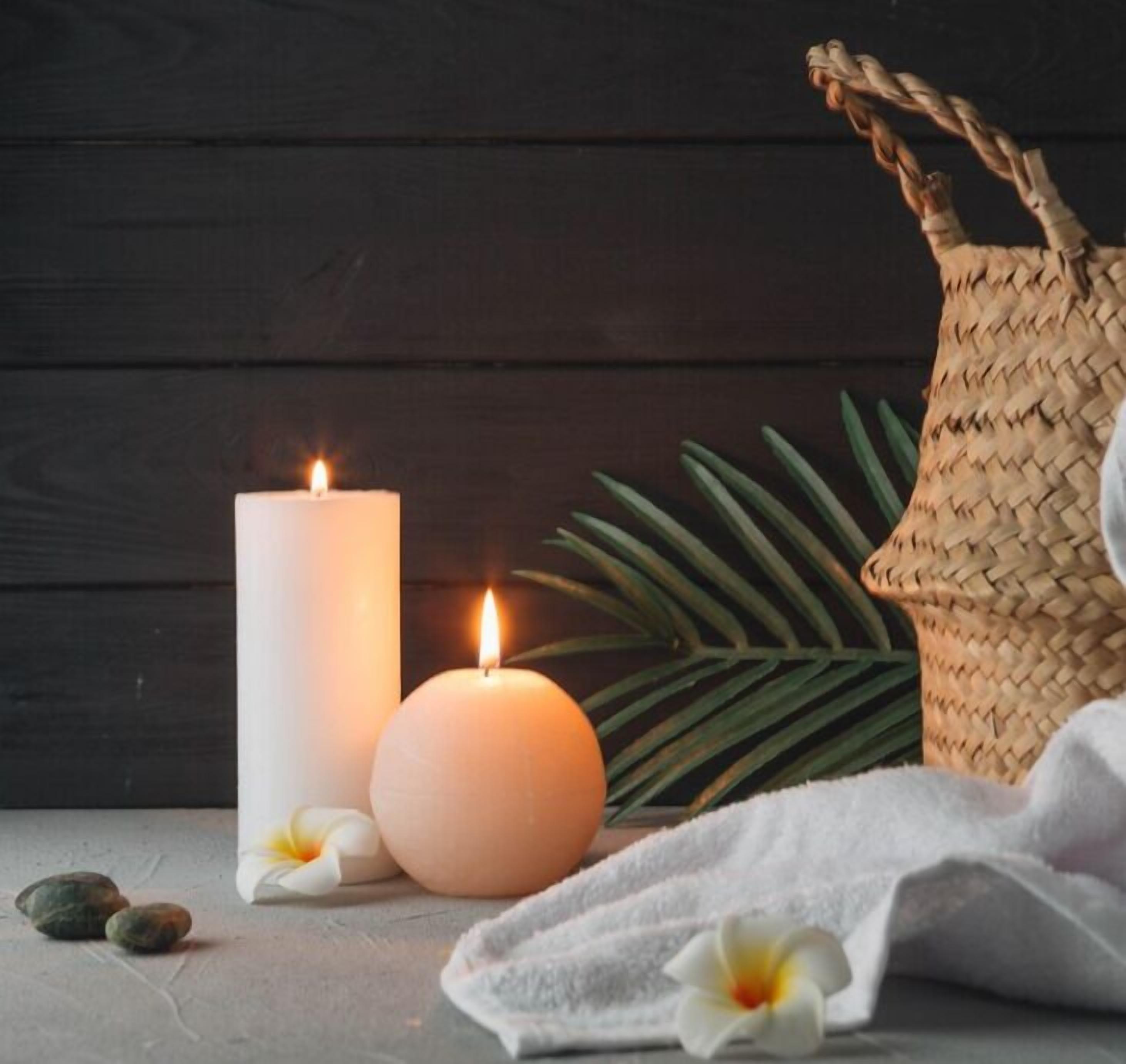 A candle, a small round candle, and a woven basket on a wooden surface.
