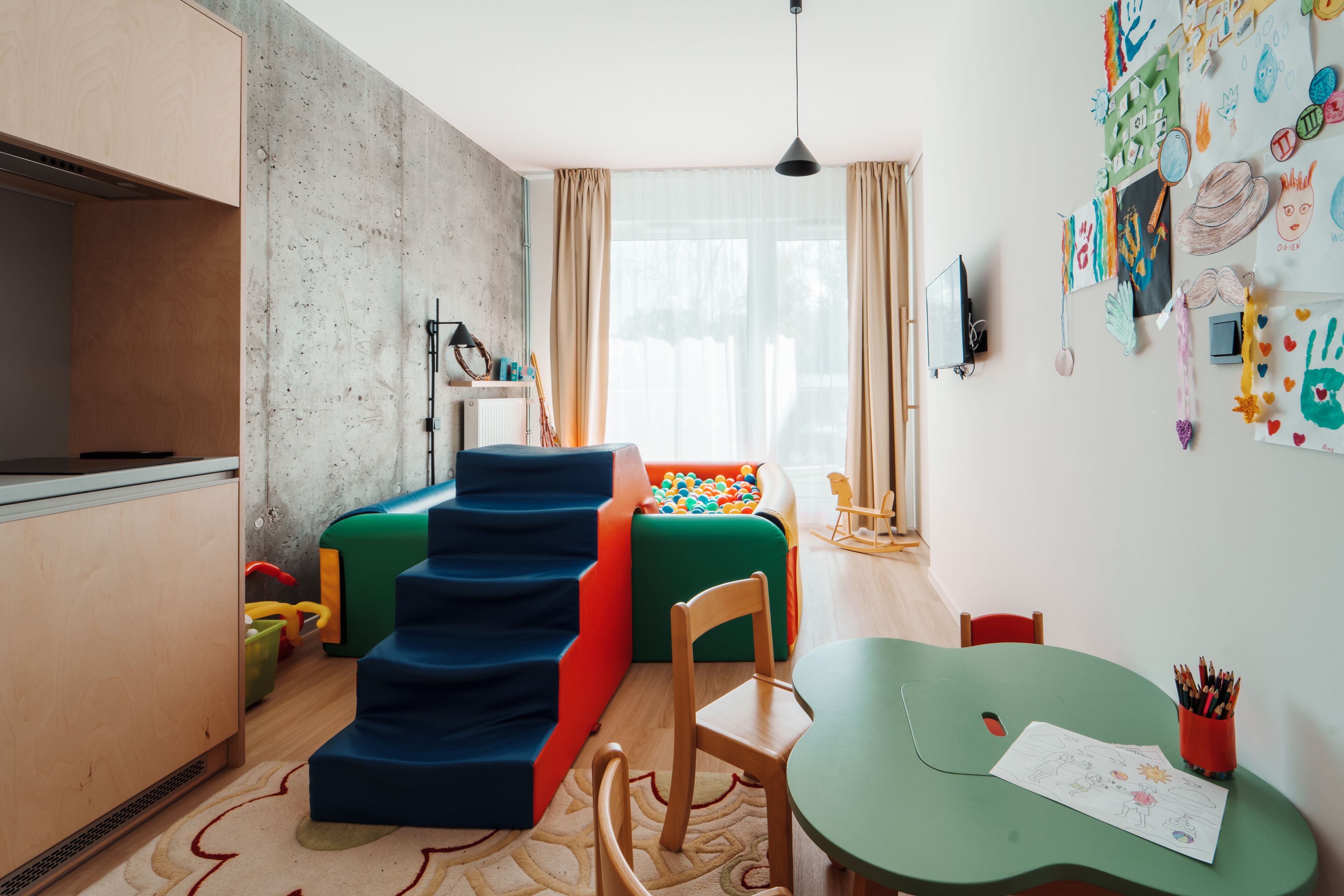 A child's play area with colorful stairs, a play table, and a wall decorated with children's drawings.
