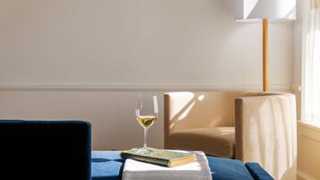 Une pièce avec une chaise bleue, une table sur laquelle se trouve un livre et un verre de vin blanc, et une lampe.