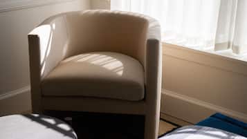 A beige armchair with a cushioned seat and backrest, positioned near a window with sheer curtains.
