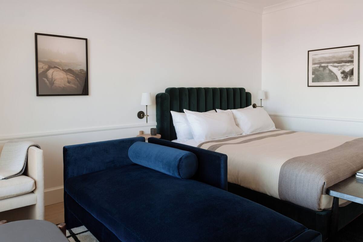 Ein Hotelzimmer mit einem Bett, einem blauen Sofa, einem Sessel und zwei gerahmten Bildern an der Wand.