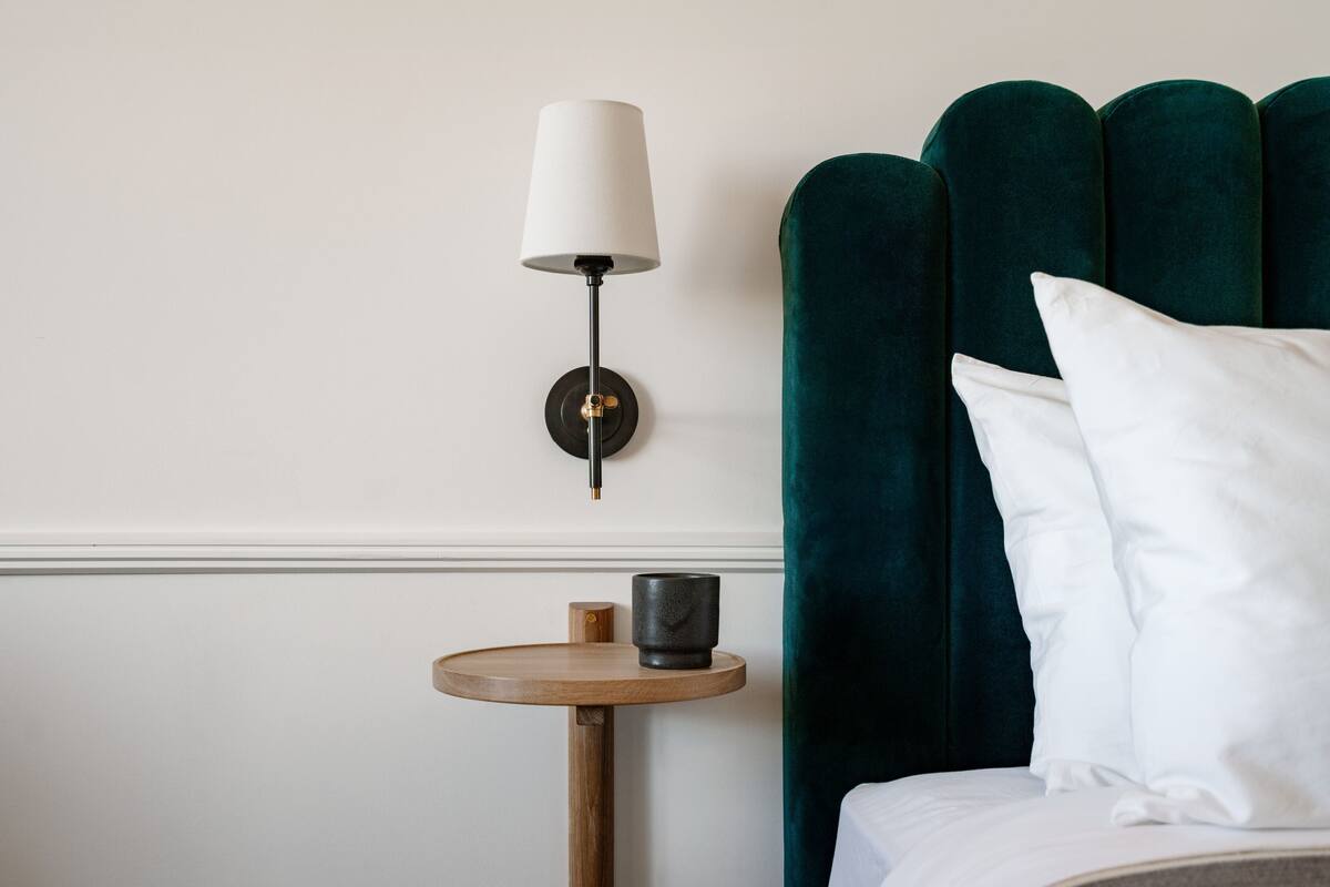 Ein ordentlich eingerichtetes Hotelzimmer mit einem Bett, einem Nachttisch mit Lampe und einem grünen, gepolsterten Kopfteil.