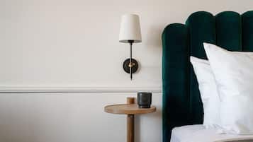A neatly arranged hotel room with a bed, a bedside table with a lamp, and a green upholstered headboard.
