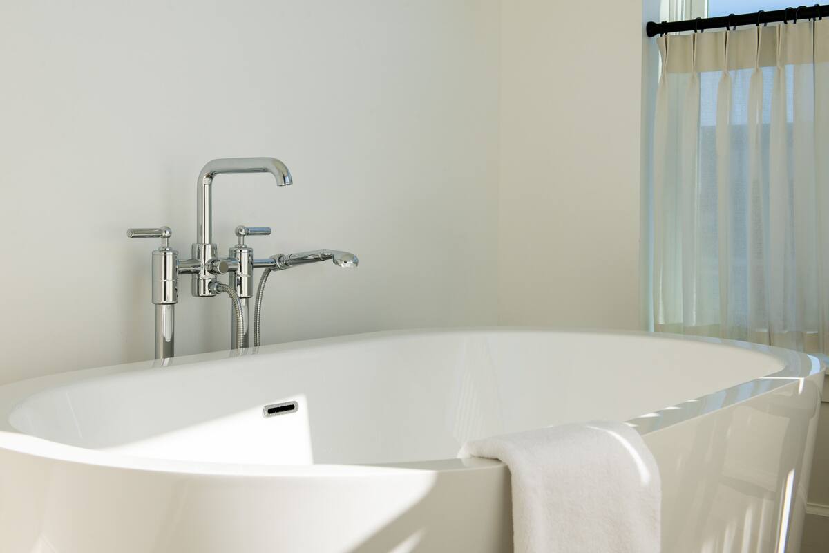 Eine moderne Badewanne mit chromfarbenen Wasserhahn und Duschkopf, einem Bedienknopf und einem Handtuch über der Seite.