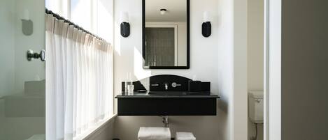 Un baño con un lavabo negro, un espejo y un perchero para toallas.
