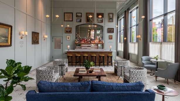 A modern bar area with a counter and stools, surrounded by patterned chairs and a blue sofa. - Longfellow Hotel (Portland)