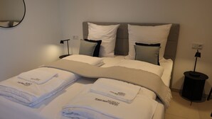 A neatly made bed with white linens and a grey blanket, two bedside tables with lamps, and a wall-mounted mirror. - 1 Doppelbett Zimmer 21 (München)
