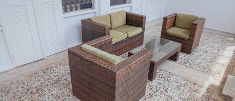 A corner seating area with wicker furniture and a glass table, set on a terrazzo floor.