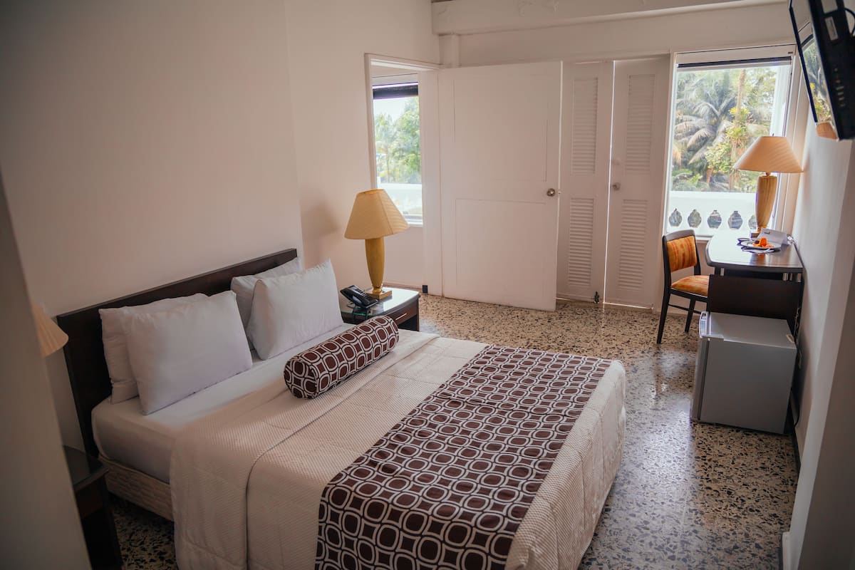 Une chambre d’hôtel comprenant un lit, un bureau avec une lampe, une chaise et un petit réfrigérateur.