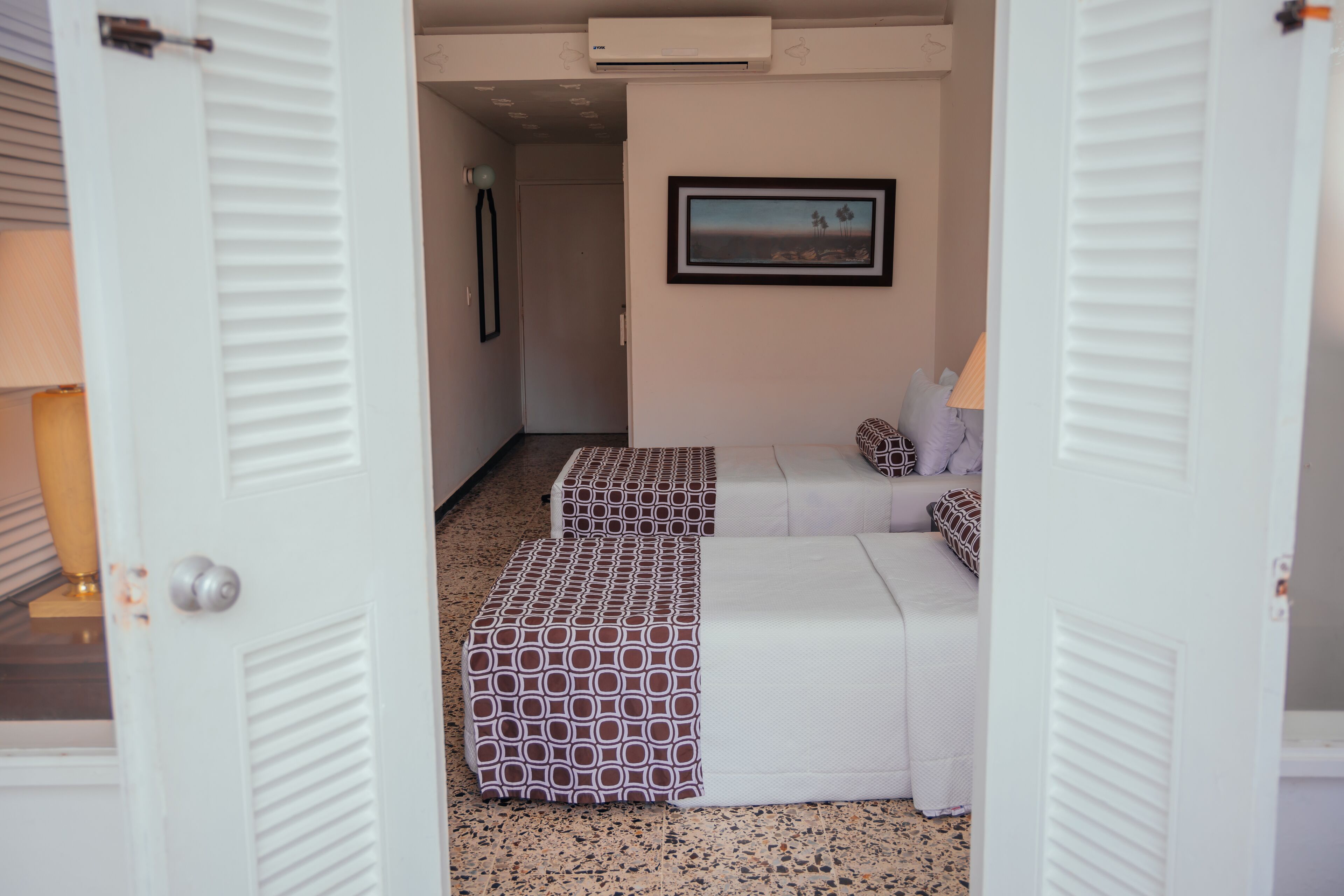Una habitación de hotel con una cama blanca, un reposapiés estampado y un cuadro en la pared.