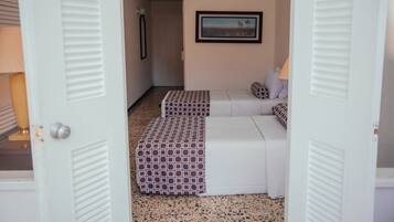 Una habitación de hotel con una cama blanca, un reposapiés estampado y un cuadro en la pared.