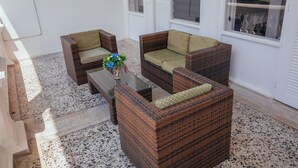 A seating area with wicker furniture and a glass table, featuring a terrazzo floor and white walls. - Hotel Estación by Destino Pacifico (Buenaventura)