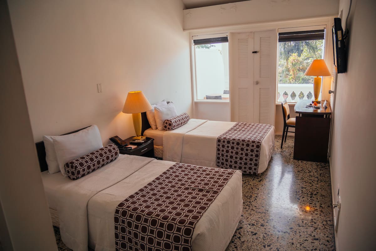 Une chambre d’hôtel avec deux lits, un bureau avec une chaise, une fenêtre donnant sur un paysage agréable et une porte.