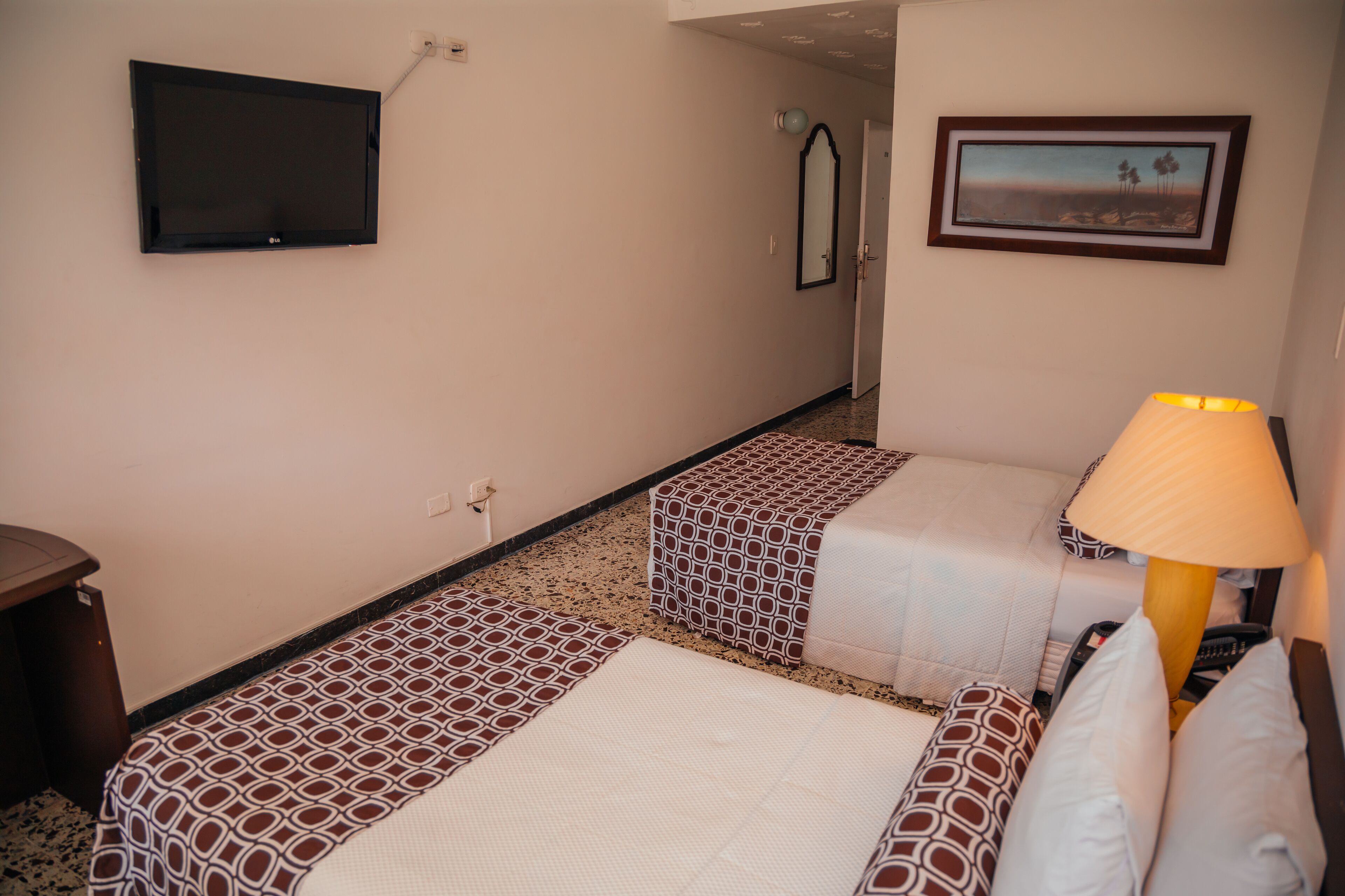 A hotel room with two beds, a TV, a framed picture on the wall, and a lamp.
