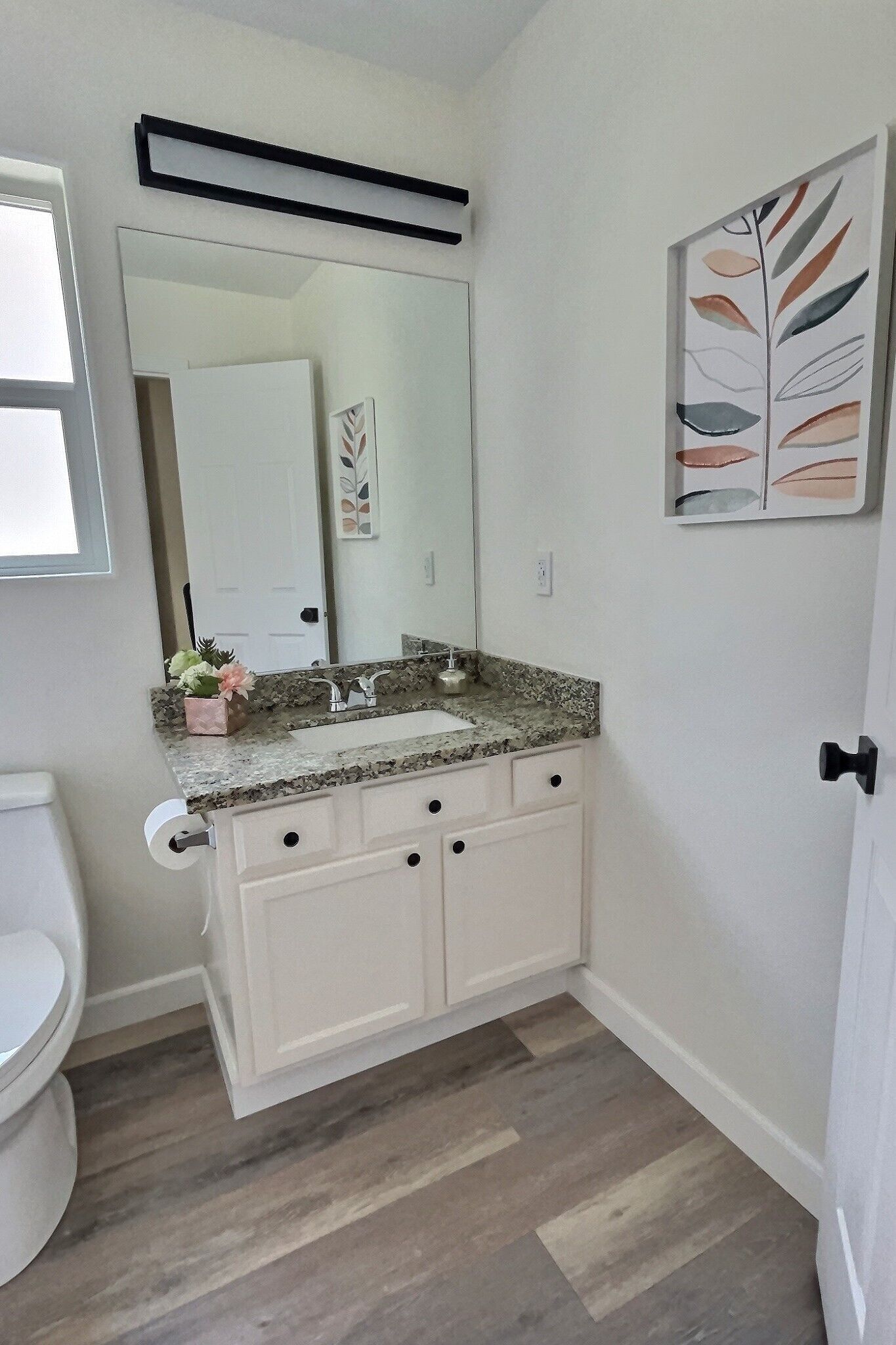 Une salle de bain avec un meuble-lavabo blanc, un plan de travail en granit et un grand miroir.
