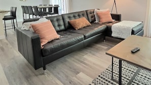 Un salon moderne avec un canapé en cuir noir, une table basse en bois et un coin repas comprenant une table et des chaises.