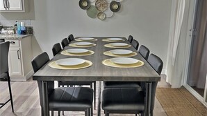 Un coin repas avec une table rectangulaire dressée pour six personnes, des chaises noires et un élément décoratif mural au-dessus.