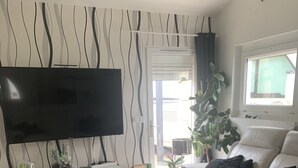 A modern living room with a flat-screen TV, a glass coffee table, a sofa, and a bookshelf.