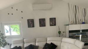 A modern living room with a white sectional sofa, a glass coffee table, and a white air conditioning unit on the wall.
