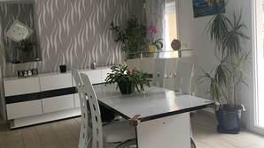 A modern kitchen with a dining area, featuring a white and black color scheme, wooden flooring, and various potted plants.