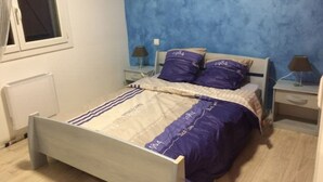 A bedroom with a bed, two bedside tables, a window, and a radiator.
