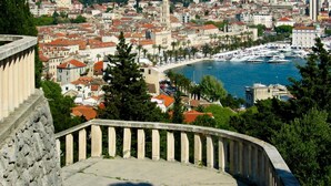 Paesaggio costiero con un porto turistico, edifici storici e una scalinata in pietra.
