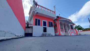 Un edificio de dos pisos con fachada roja y blanca, un balcón y una entrada pequeña.