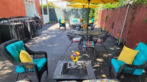 Une terrasse extérieure avec des meubles en osier, une table ronde et un parasol jaune.