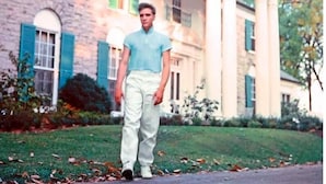 Un homme se tient devant un grand bâtiment à deux étages, de style architectural classique, avec un portique à colonnes et une façade en pierre.