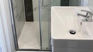 Un baño con ducha de vidrio y un lavabo blanco con grifo cromado.