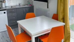 Una cocina funcional con una mesa blanca y sillas naranjas, un fregadero y una ventana con cortinas amarillas.