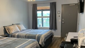 Een hotelkamer met twee bedden, een plafondventilator, een raam met gordijnen, een deur en een kitchenette.
