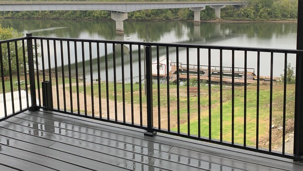 Uitzicht vanuit een overdekt balkon op een rivier met een brug, grasvelden en enkele industriële gebouwen.