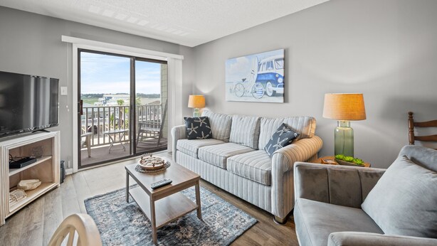 A living room with a sofa, a coffee table, a TV, and a balcony with a view.